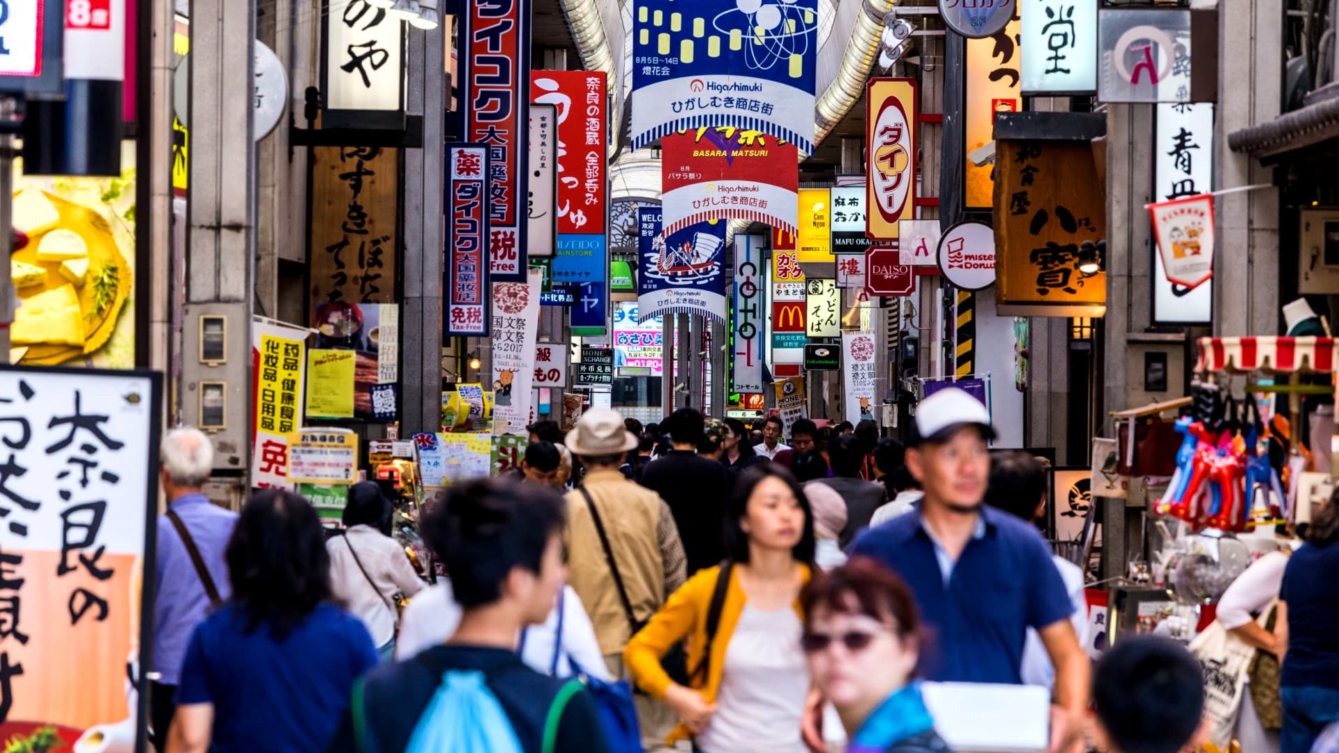 Crowd of people walking through a bustling street market filled with colorful signs in Japan. - Olive Oil Times