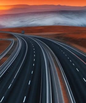 A highway winding through a mountainous landscape during sunset with orange and purple hues in the sky. - Olive Oil Times