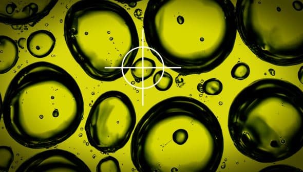 Close-up image of oil droplets on a yellow background with a focus circle overlay. - Olive Oil Times
