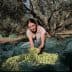 Woman holding freshly harvested olives while sitting on a green net in an olive grove. - Olive Oil Times