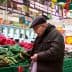 An elderly man examining vegetables in a grocery store with green produce bins. - Olive Oil Times