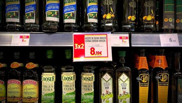 Various bottles of olive oil displayed on a supermarket shelf with pricing labels. - Olive Oil Times