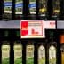 Various bottles of olive oil displayed on a supermarket shelf with pricing labels. - Olive Oil Times