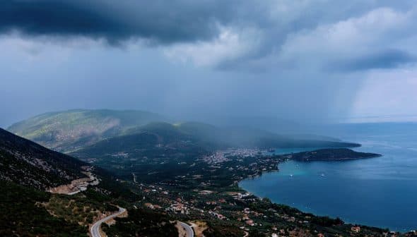 A coastal landscape featuring mountains, a bay, and cloudy skies over the water. - Olive Oil Times