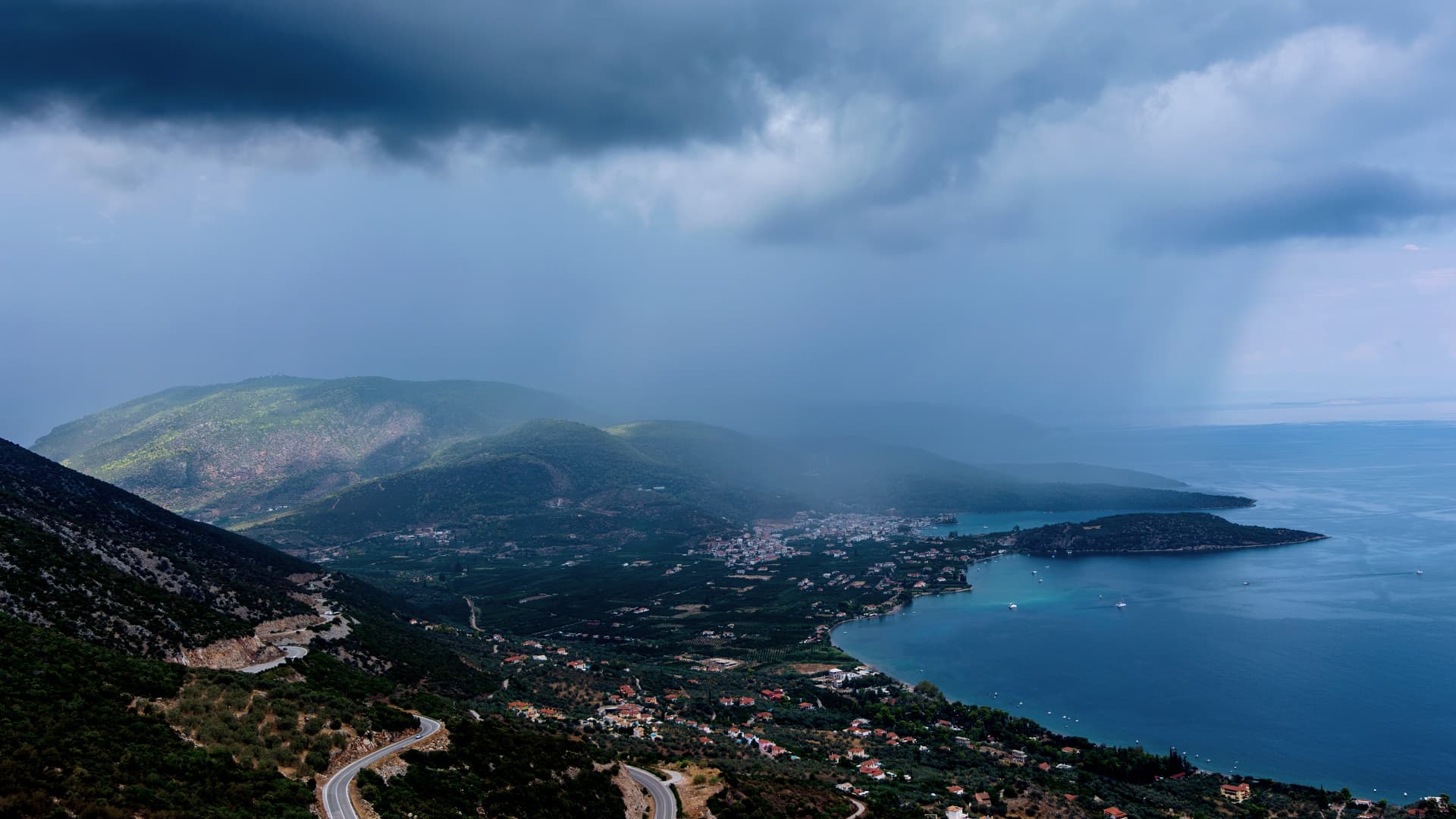 A coastal landscape featuring mountains, a bay, and cloudy skies over the water. - Olive Oil Times