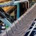 Industrial conveyor belt system with multiple inclined belts and metal framework. - Olive Oil Times
