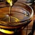 Golden olive oil being poured into a glass bowl placed on a wooden surface. - Olive Oil Times