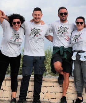 Four individuals posing together outdoors, wearing matching t-shirts and smiling at the camera. - Olive Oil Times