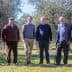 Six men standing together in an olive grove, dressed in casual and formal attire. - Olive Oil Times