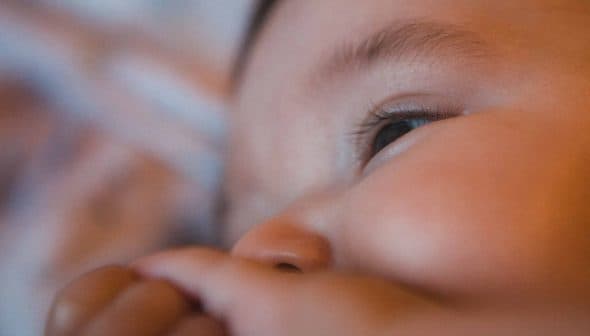 Close-up view of a baby's face with a focus on the eye and hand. - Olive Oil Times