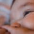 Close-up view of a baby's face with a focus on the eye and hand. - Olive Oil Times