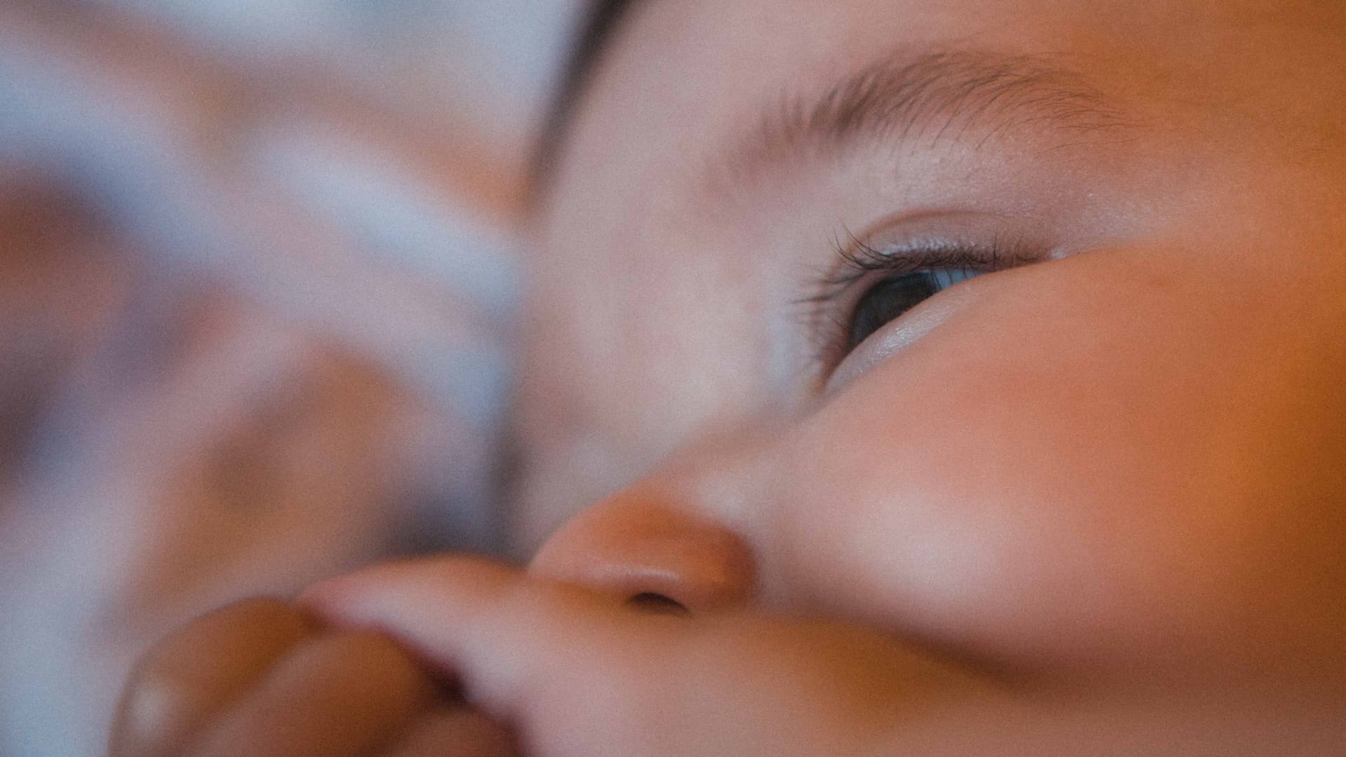 Close-up view of a baby's face with a focus on the eye and hand. - Olive Oil Times