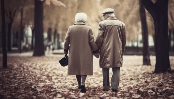 An elderly couple holding hands while walking through a park covered in autumn leaves. - Olive Oil Times