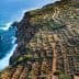 Aerial view of terraced agricultural fields along a coastal cliff with ocean waves below. - Olive Oil Times