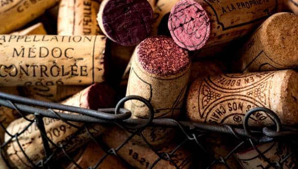 Various wine corks with different colors and markings placed in a wire basket. - Olive Oil Times