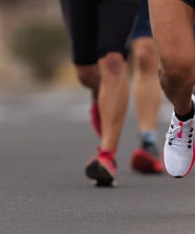 Close-up of a runner's foot in athletic shoes on a road with other runners in the background. - Olive Oil Times