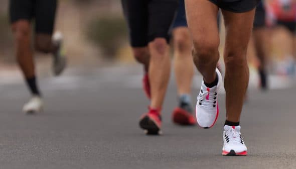 Close-up of a runner's foot in athletic shoes on a road with other runners in the background. - Olive Oil Times