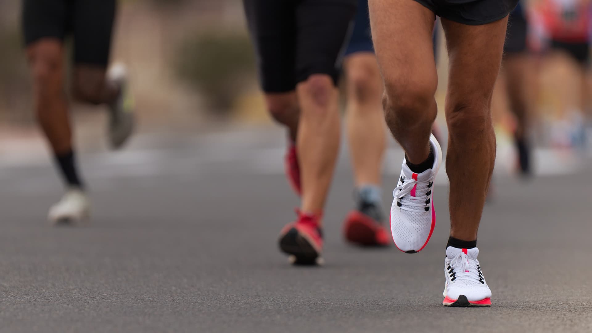 Close-up of a runner's foot in athletic shoes on a road with other runners in the background. - Olive Oil Times