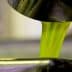 Green olive oil pouring from a metal spout into a container. - Olive Oil Times