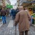 Elderly man with a cane walking through a market street lined with stalls and produce. - Olive Oil Times