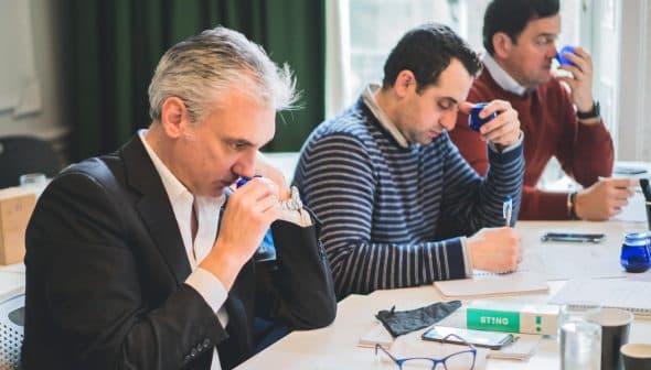 Three men participating in a tasting session, focusing on their individual tasks and using tasting tools. - Olive Oil Times