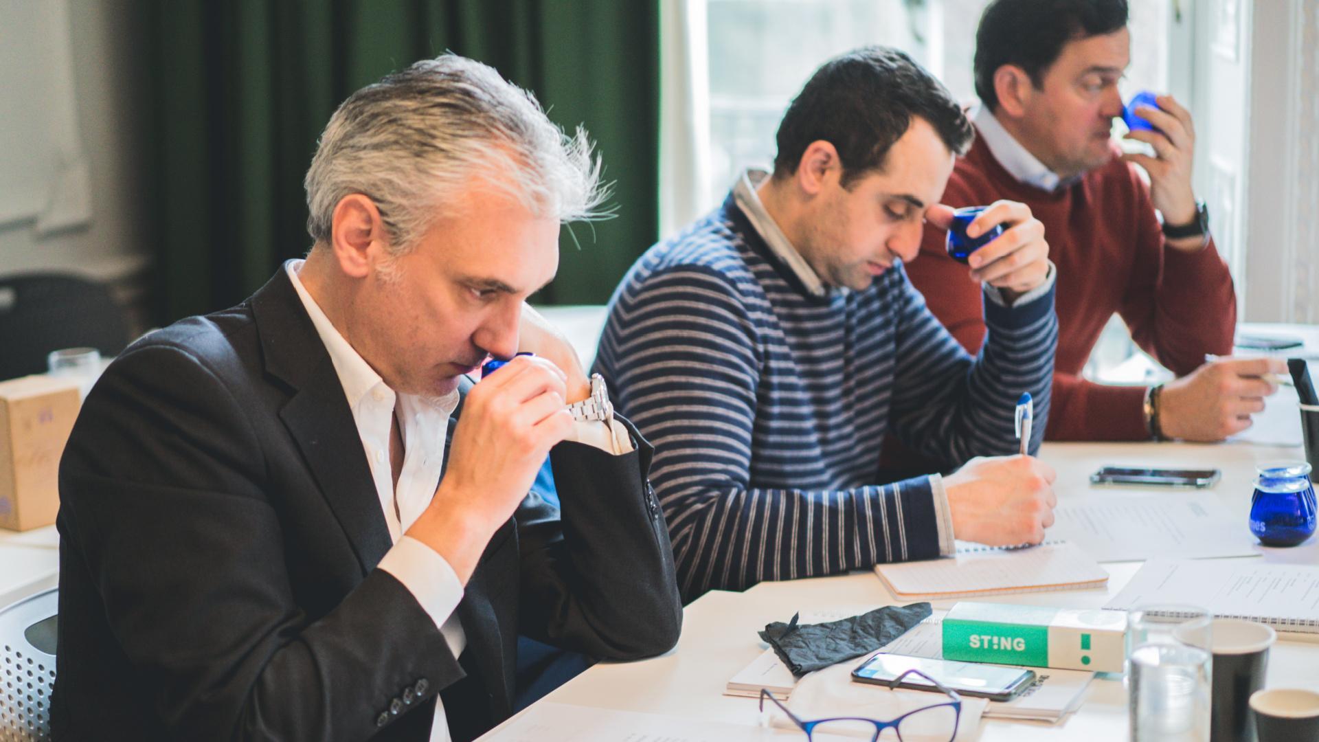 Three men participating in a tasting session, focusing on their individual tasks and using tasting tools. - Olive Oil Times