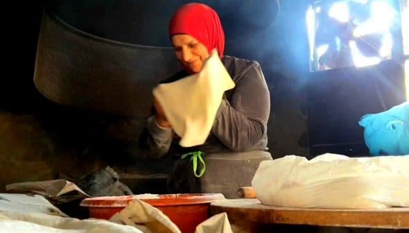 A woman wearing a red headscarf is preparing dough in a kitchen setting. - Olive Oil Times