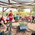 A group of children and adults seated in a circular outdoor learning space with a speaker in the center. - Olive Oil Times