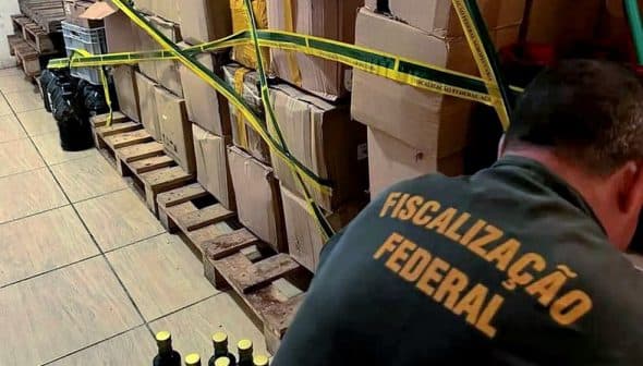 Boxes and bottles secured with yellow tape in a storage area with a person inspecting them. - Olive Oil Times