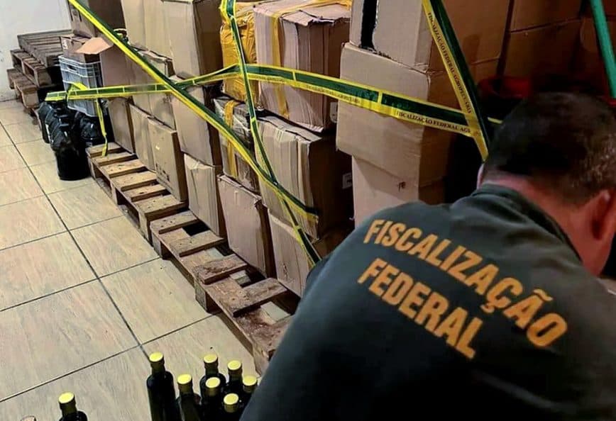 Boxes and bottles secured with yellow tape in a storage area with a person inspecting them. - Olive Oil Times