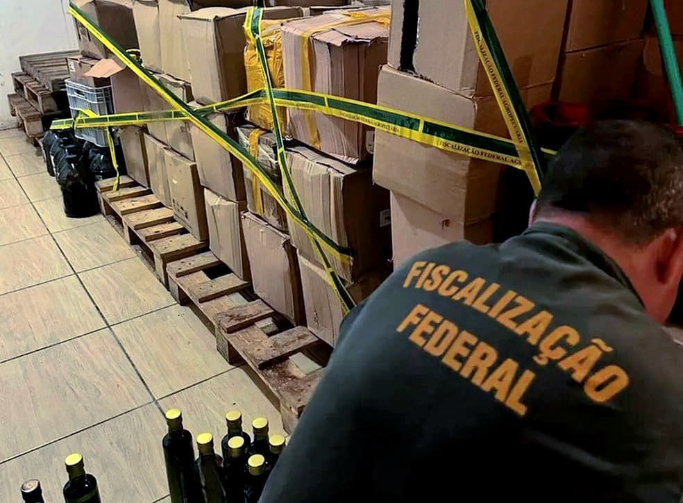 Boxes and bottles secured with yellow tape in a storage area with a person inspecting them. - Olive Oil Times