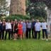 A group of individuals posing together for a photo in an outdoor area with greenery and a stone structure. - Olive Oil Times