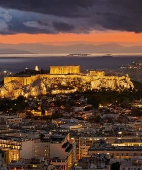 View of the Acropolis of Athens illuminated at sunset with a colorful sky and distant mountains. - Olive Oil Times