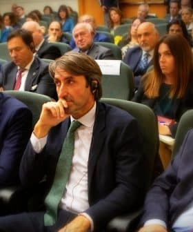 A group of individuals seated in a conference setting, some wearing headphones and engaged in discussion. - Olive Oil Times