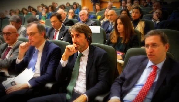 A group of individuals seated in a conference setting, some wearing headphones and engaged in discussion. - Olive Oil Times