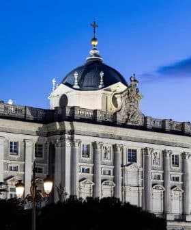 The Royal Palace of Madrid with a domed roof and decorative architecture illuminated at dusk. - Olive Oil Times