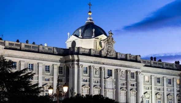 The Royal Palace of Madrid with a domed roof and decorative architecture illuminated at dusk. - Olive Oil Times