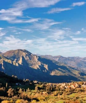 Scenic view of mountains with a small village nestled in the valley under a blue sky. - Olive Oil Times