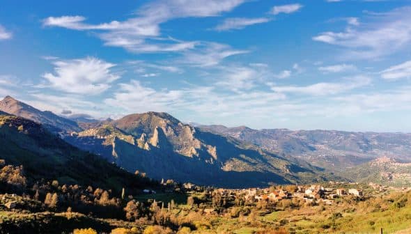 Scenic view of mountains with a small village nestled in the valley under a blue sky. - Olive Oil Times