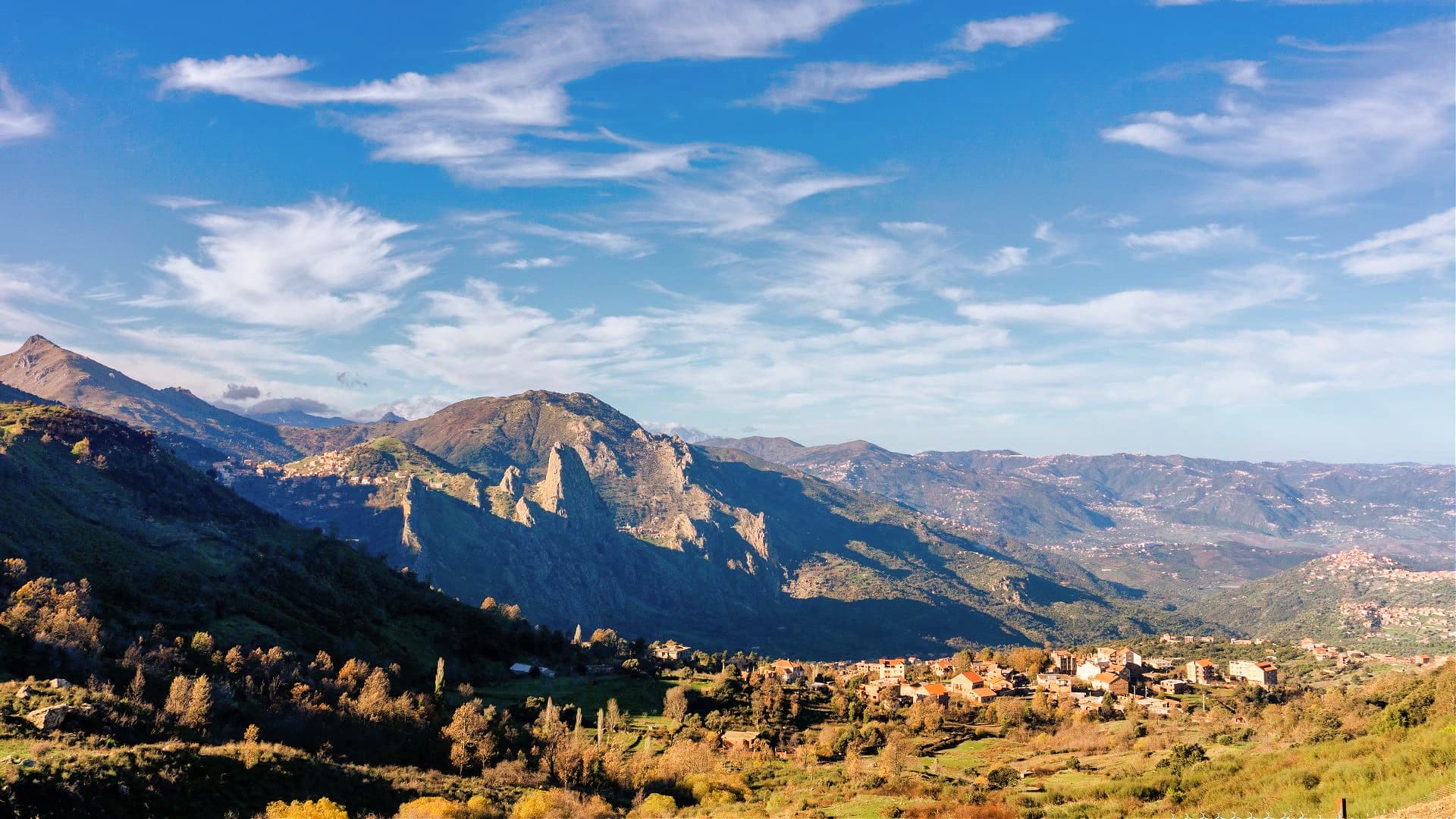 Scenic view of mountains with a small village nestled in the valley under a blue sky. - Olive Oil Times
