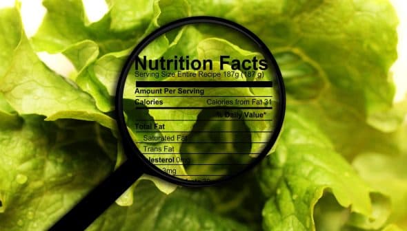 Magnifying glass focusing on nutrition facts label on leafy greens background. - Olive Oil Times