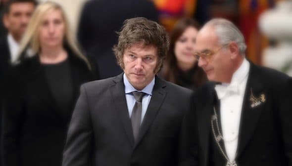 Two men in formal attire walking together at an event, one wearing a suit and tie, the other in a tuxedo. - Olive Oil Times