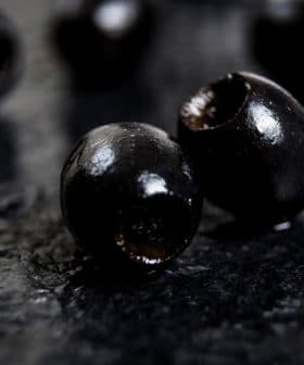 Close-up of black olives placed on a dark textured surface. - Olive Oil Times