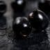 Close-up of black olives placed on a dark textured surface. - Olive Oil Times