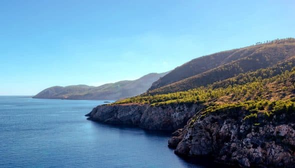 Coastal view featuring cliffs and calm water under a clear blue sky. - Olive Oil Times