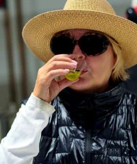 Woman wearing a straw hat and sunglasses tasting olive oil in a factory setting. - Olive Oil Times