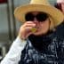 Woman wearing a straw hat and sunglasses tasting olive oil in a factory setting. - Olive Oil Times