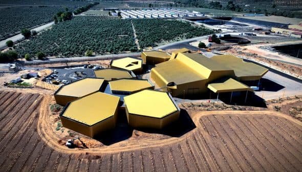 Aerial view of a modern olive oil processing facility with a hexagonal design and yellow roofs. - Olive Oil Times