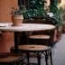 A round table with a potted plant and three chairs in a narrow outdoor setting. - Olive Oil Times