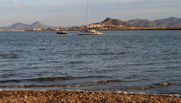 Two sailboats anchored on calm water with mountains visible in the background. - Olive Oil Times